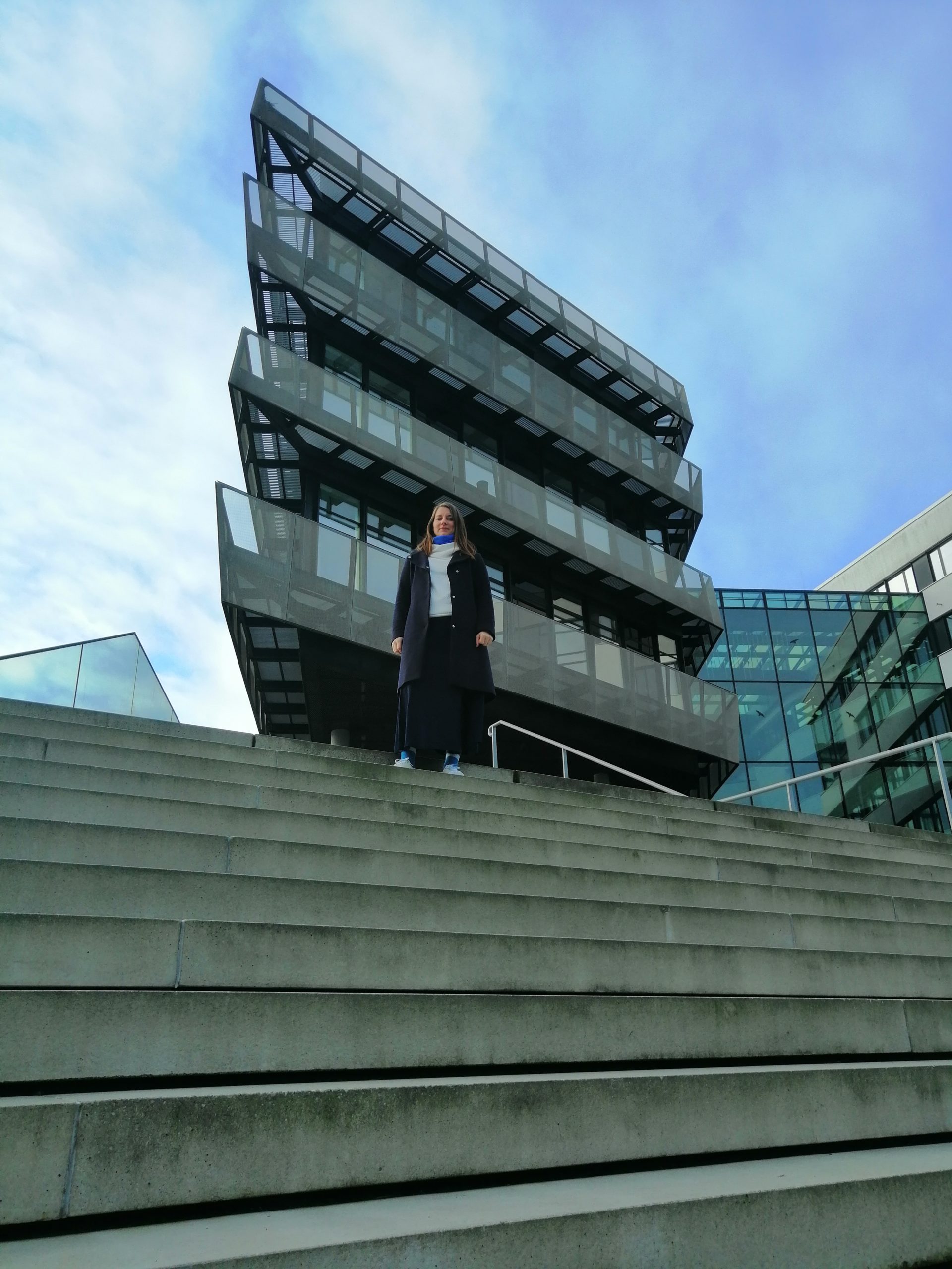 Mirja steht vor einem Firmengebäude auf einer Treppe.
