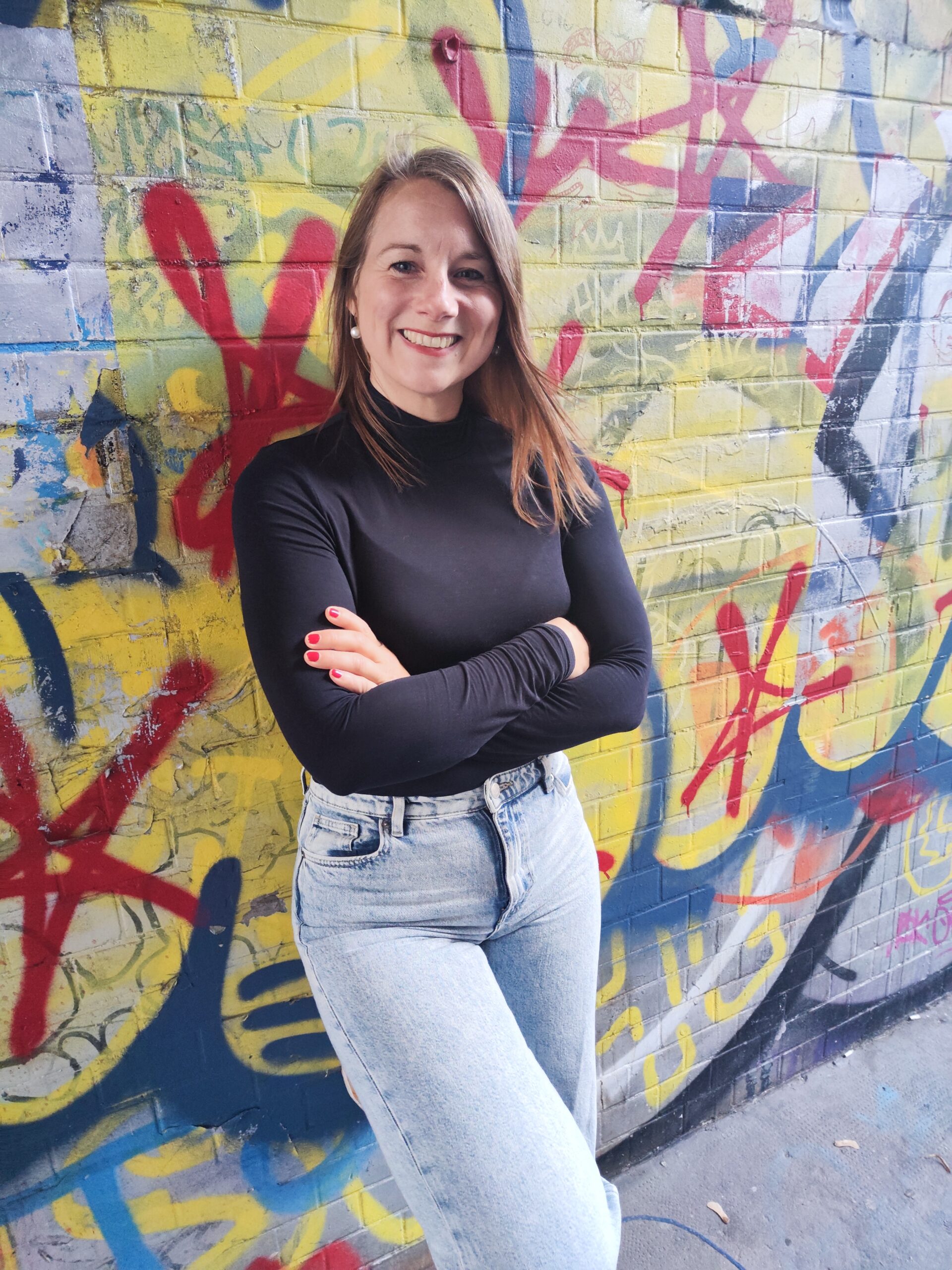 Mirja Graffitiwand Mirja steht vor einer bunten Graffiti Wand