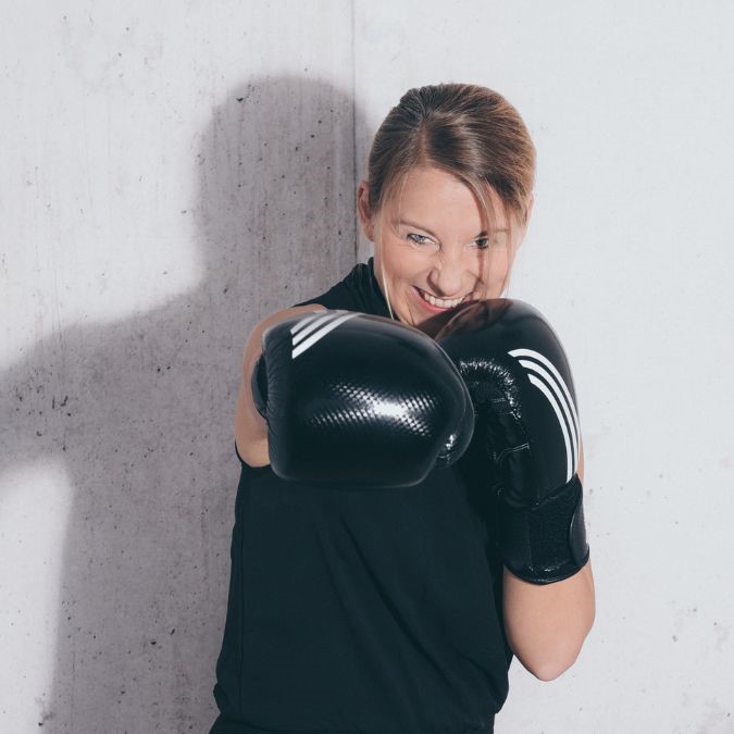 Mirja steht frontal mit Boxhandschuhen in Boxpose und lächelt-