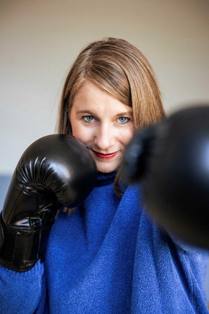 Mirja Grüter in Boxpose mit schwarzen Handschuhen, trägt blauen Pullover und lächelt selbstbewusst